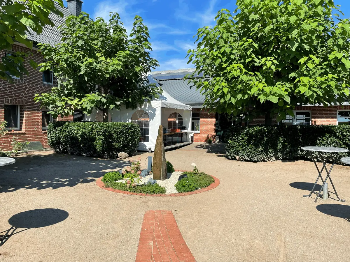 Biergarten mit Springbrunnen, Stehtischen und Bäumen vor dem Bistro