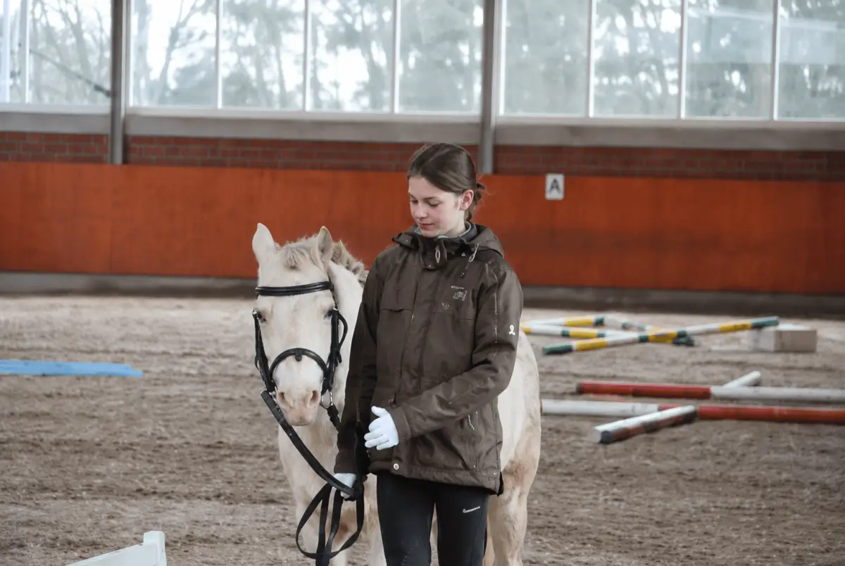 Jugendliche Reitschülerin führt helles Pony durch die Reithalle der Reitsportanlage Hollmann-Raabe in Bielefeld